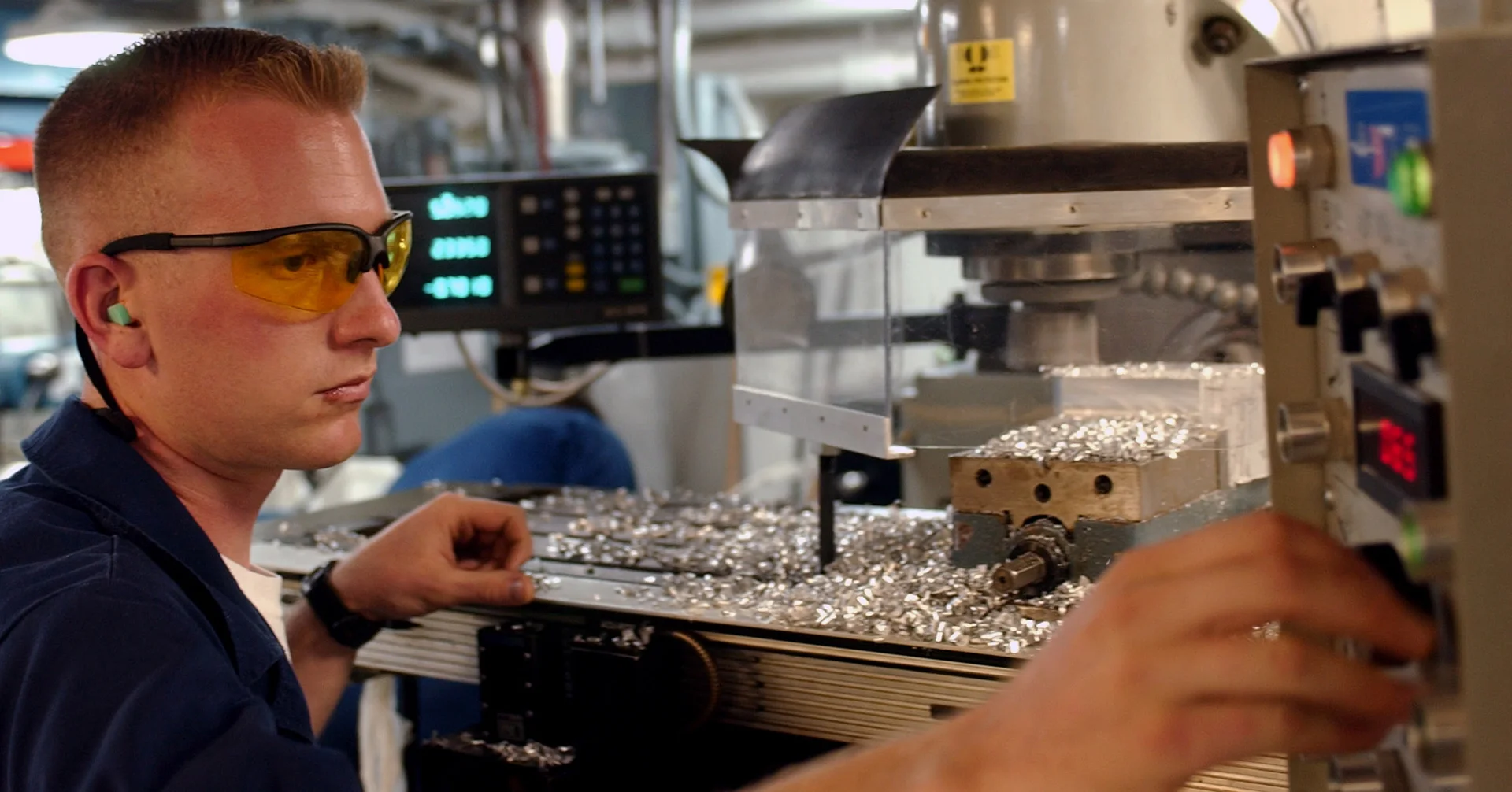 An operator wearing safety glasses working at a milling machine in a workshop.