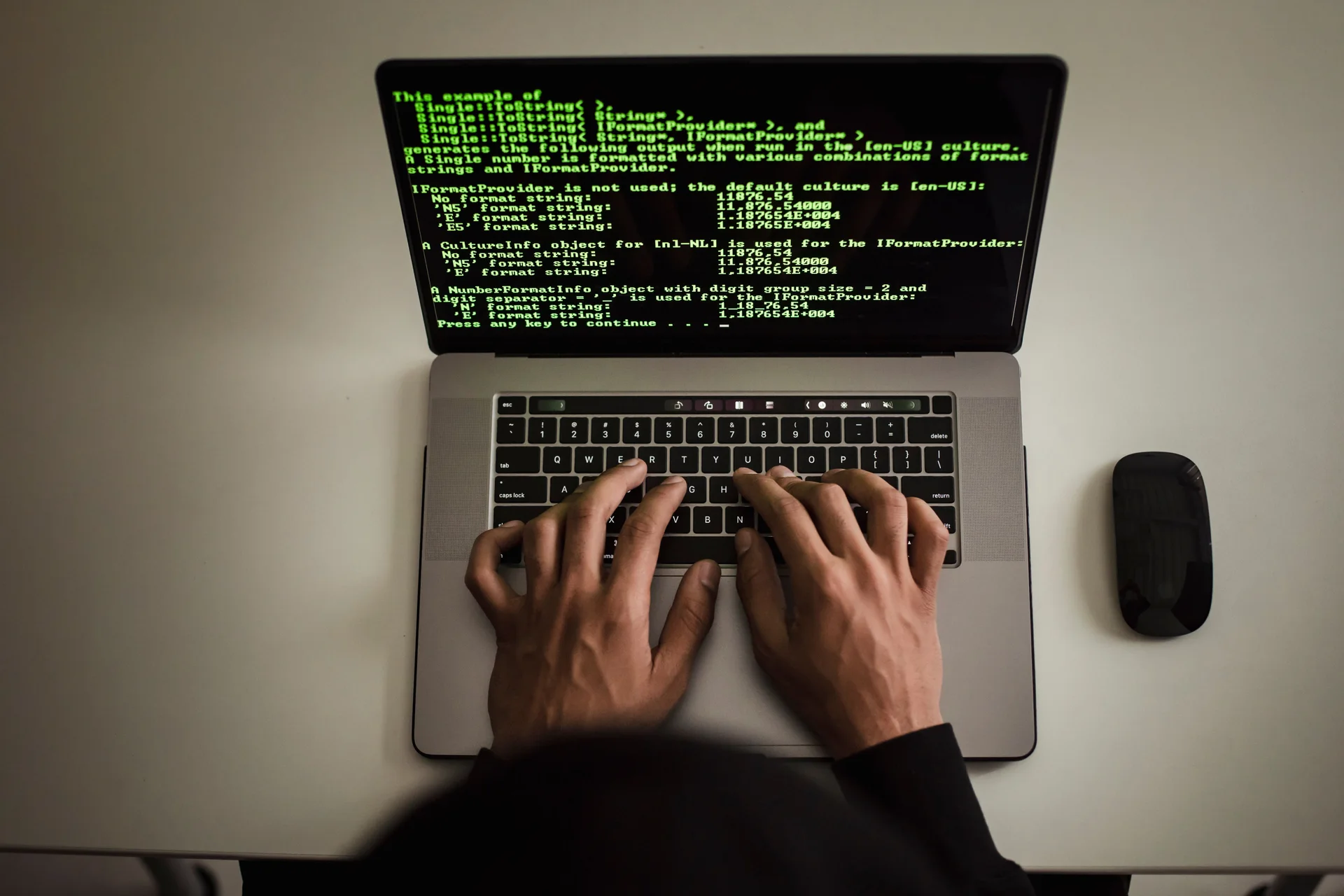 Overhead view of hands on a laptop keyboard; the screen displays green text showing output from a programming example.